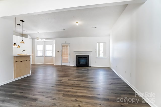 unfurnished living room featuring a fireplace with flush hearth, baseboards, lofted ceiling, ceiling fan, and dark wood-type flooring