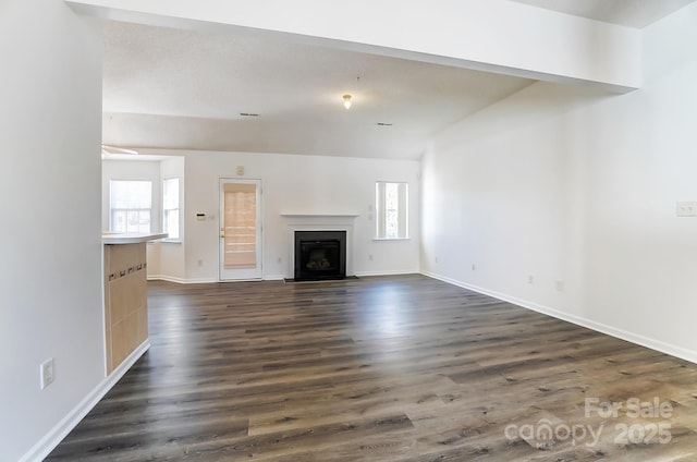 unfurnished living room featuring baseboards, a glass covered fireplace, a wealth of natural light, and dark wood-style floors