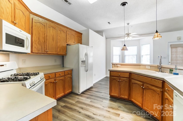 kitchen featuring vaulted ceiling, a sink, brown cabinets, white appliances, and pendant lighting