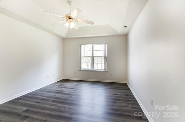 spare room with ceiling fan, a tray ceiling, visible vents, baseboards, and dark wood-style flooring