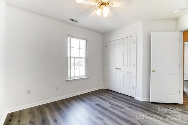 unfurnished bedroom with wood finished floors, a closet, ceiling fan, baseboards, and visible vents