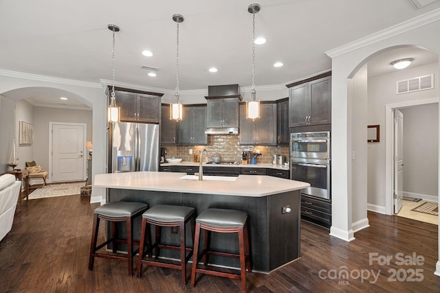 kitchen featuring appliances with stainless steel finishes, hanging light fixtures, backsplash, dark brown cabinetry, and an island with sink