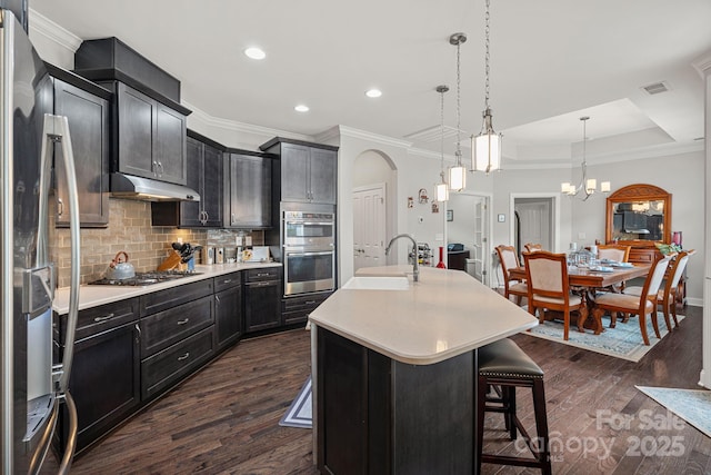 kitchen featuring appliances with stainless steel finishes, an island with sink, sink, a breakfast bar area, and hanging light fixtures