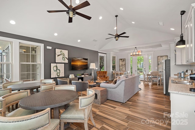 living room featuring wood-type flooring, sink, ceiling fan with notable chandelier, and high vaulted ceiling