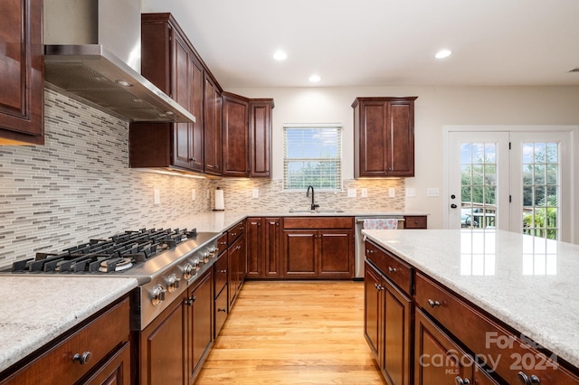 kitchen with tasteful backsplash, sink, wall chimney exhaust hood, light hardwood / wood-style flooring, and light stone countertops