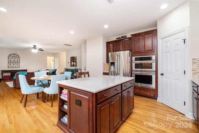 kitchen with appliances with stainless steel finishes, light hardwood / wood-style floors, tasteful backsplash, a center island, and ceiling fan