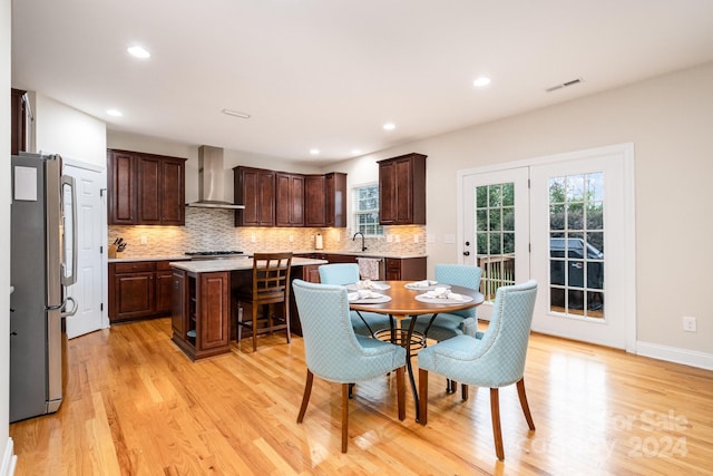 kitchen featuring light hardwood / wood-style flooring, backsplash, wall chimney range hood, appliances with stainless steel finishes, and a center island