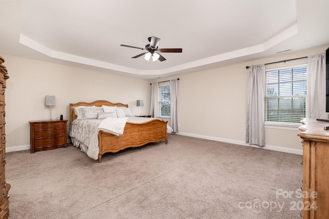 carpeted bedroom with ceiling fan and a raised ceiling