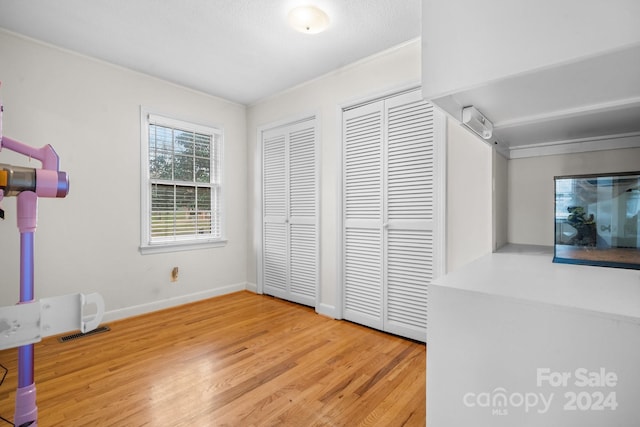 unfurnished bedroom featuring hardwood / wood-style floors, ornamental molding, and two closets