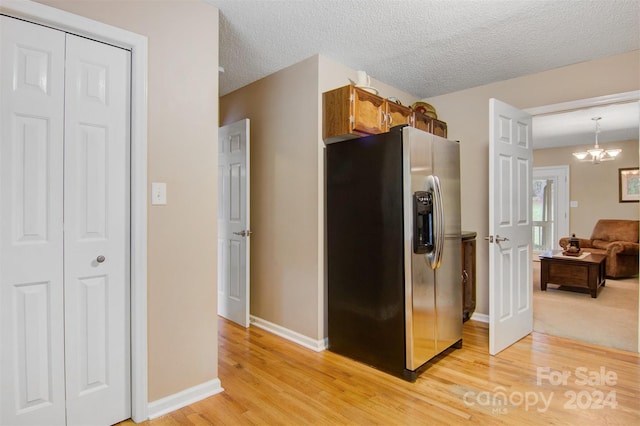 kitchen featuring a textured ceiling, light hardwood / wood-style floors, a notable chandelier, decorative light fixtures, and stainless steel fridge