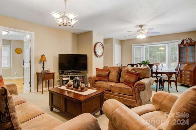 carpeted living room featuring a healthy amount of sunlight, ceiling fan with notable chandelier, and a textured ceiling