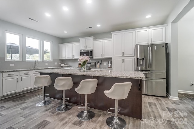 kitchen featuring appliances with stainless steel finishes, a kitchen island with sink, hardwood / wood-style floors, and white cabinets