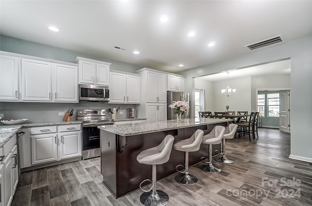 kitchen featuring appliances with stainless steel finishes, white cabinets, a center island, hardwood / wood-style flooring, and a chandelier