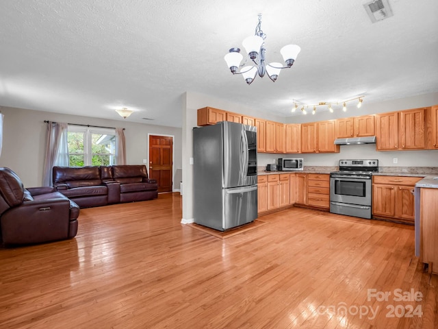 kitchen with appliances with stainless steel finishes, an inviting chandelier, a textured ceiling, and light hardwood / wood-style floors