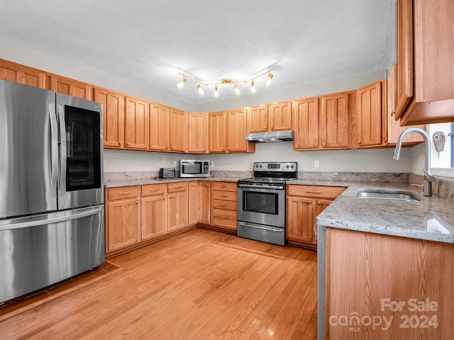 kitchen featuring sink, light wood-type flooring, a textured ceiling, stainless steel appliances, and light stone counters