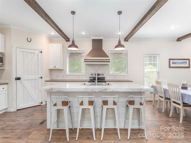 kitchen with white cabinetry, hanging light fixtures, light stone counters, and wall chimney exhaust hood