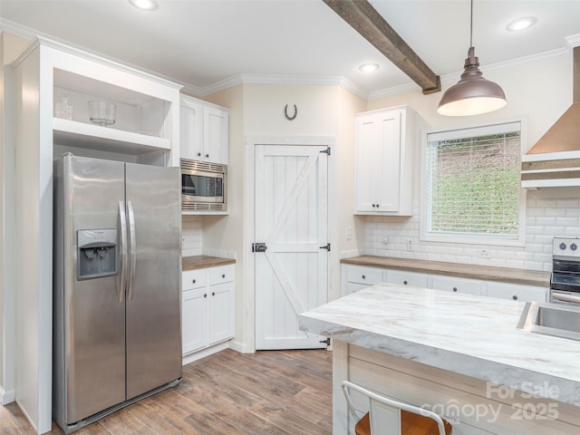 kitchen with white cabinetry, appliances with stainless steel finishes, wall chimney exhaust hood, and decorative light fixtures