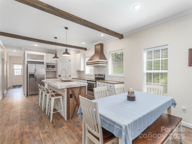 dining space featuring wood-type flooring, beam ceiling, sink, and a wealth of natural light