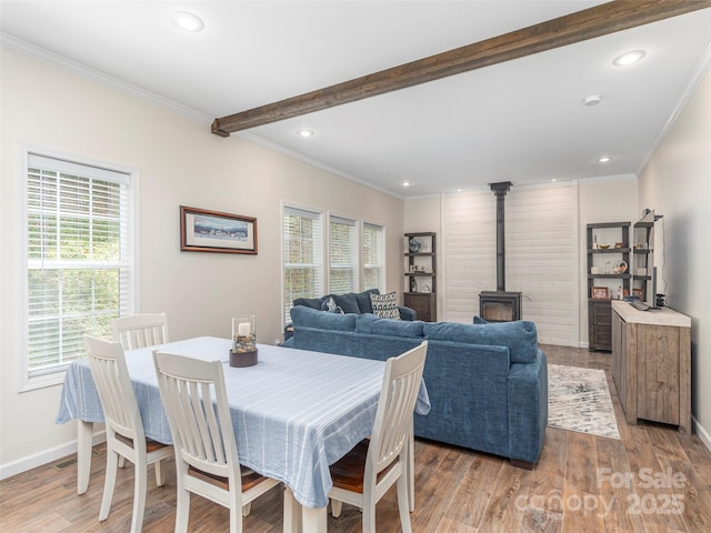 dining area featuring beam ceiling, ornamental molding, a wood stove, and light hardwood / wood-style floors