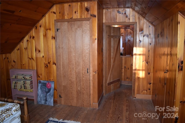 hallway featuring lofted ceiling, wooden walls, and dark wood-type flooring