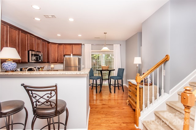 kitchen featuring light stone countertops, pendant lighting, stainless steel appliances, light wood-type flooring, and a kitchen bar