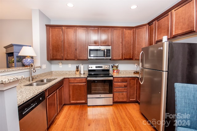 kitchen featuring light stone countertops, stainless steel appliances, light wood-type flooring, and sink