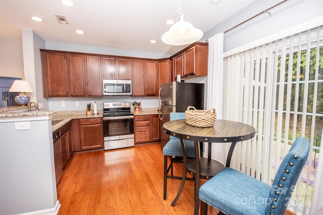 kitchen featuring appliances with stainless steel finishes, hanging light fixtures, light stone countertops, and light hardwood / wood-style flooring