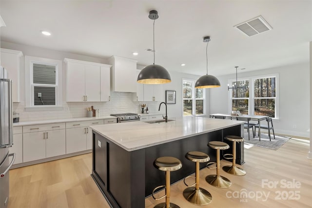 kitchen with a kitchen island with sink, sink, pendant lighting, and white cabinets