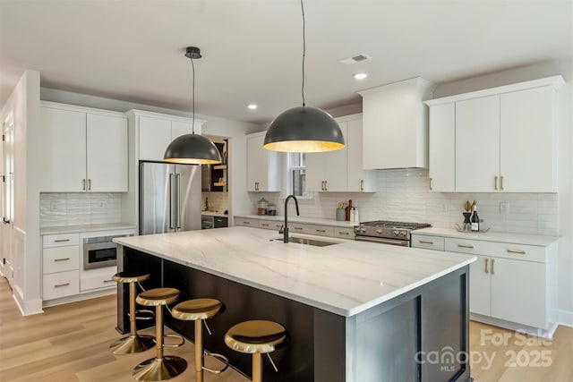 kitchen with sink, premium range hood, white cabinetry, high end appliances, and an island with sink