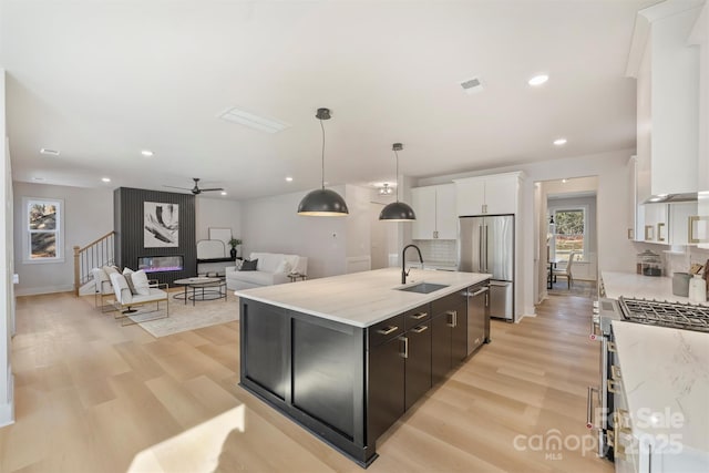 kitchen featuring sink, stainless steel appliances, an island with sink, white cabinets, and decorative light fixtures