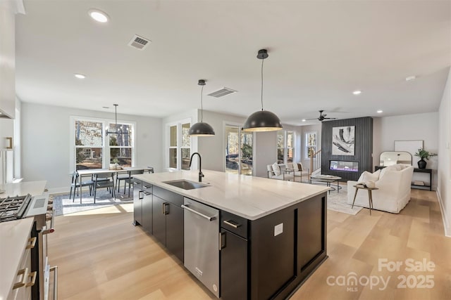 kitchen with pendant lighting, sink, light hardwood / wood-style flooring, an island with sink, and stainless steel dishwasher