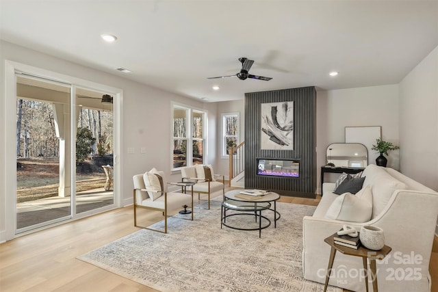 living room featuring ceiling fan, a fireplace, and light wood-type flooring