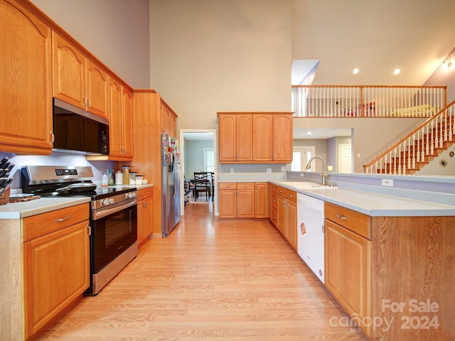 kitchen with sink, kitchen peninsula, appliances with stainless steel finishes, a towering ceiling, and light hardwood / wood-style floors