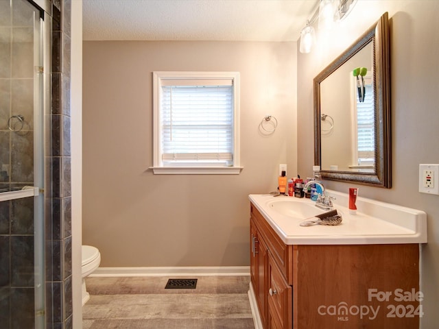 bathroom featuring a shower with door, vanity, toilet, and a textured ceiling