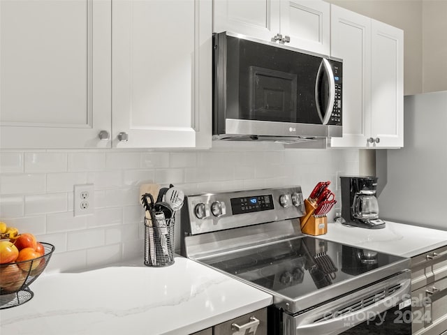 kitchen with appliances with stainless steel finishes, backsplash, light stone counters, and white cabinets