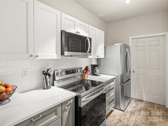 kitchen featuring appliances with stainless steel finishes, white cabinetry, light stone counters, and tasteful backsplash