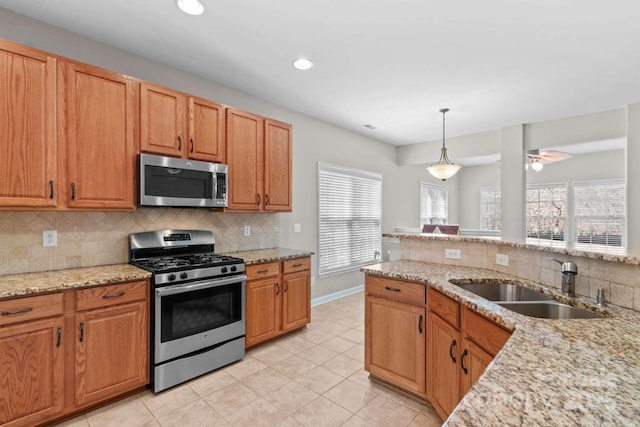 kitchen with appliances with stainless steel finishes, sink, pendant lighting, and light stone counters