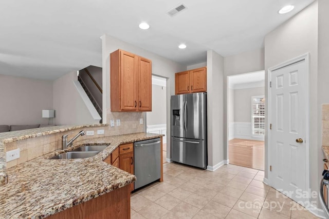 kitchen with sink, appliances with stainless steel finishes, kitchen peninsula, light stone countertops, and backsplash