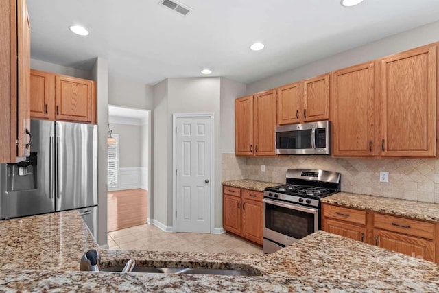 kitchen with tasteful backsplash, light tile patterned flooring, appliances with stainless steel finishes, and light stone counters