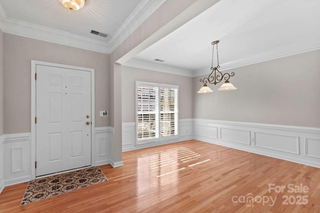 entryway with crown molding, light hardwood / wood-style floors, and a notable chandelier