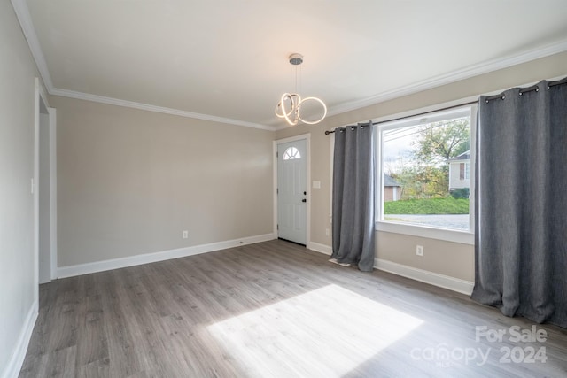 empty room featuring wood-type flooring, an inviting chandelier, and crown molding