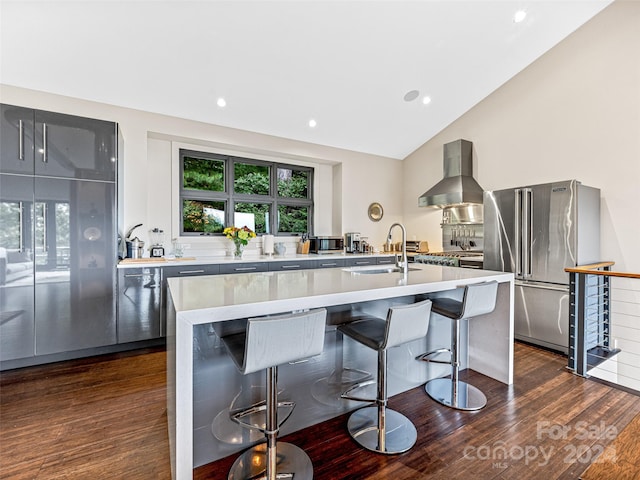 kitchen featuring an island with sink, dark wood-type flooring, high quality fridge, and wall chimney range hood