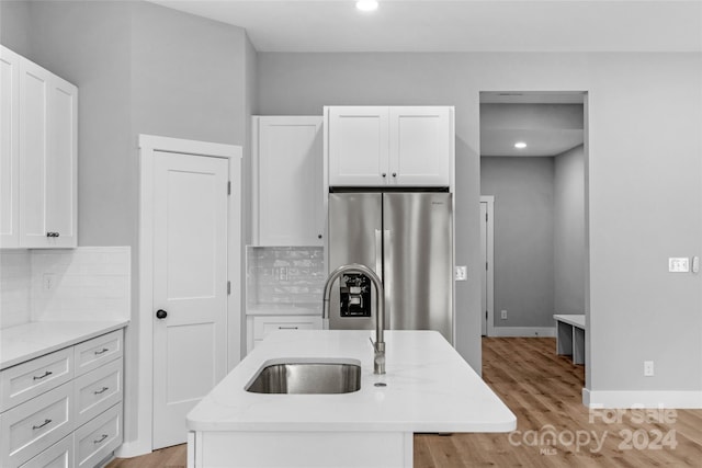 kitchen featuring decorative backsplash, light wood-type flooring, a center island with sink, sink, and stainless steel fridge with ice dispenser