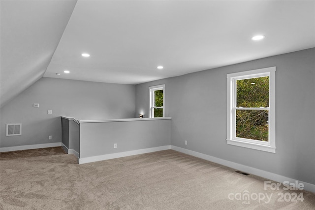 additional living space featuring light colored carpet, lofted ceiling, and plenty of natural light