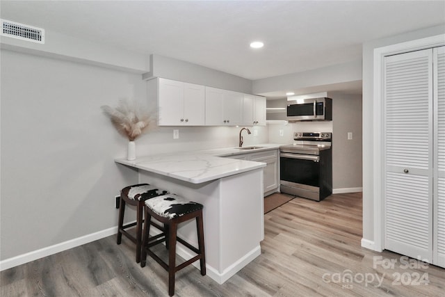 kitchen featuring light hardwood / wood-style floors, white cabinetry, kitchen peninsula, stainless steel appliances, and sink