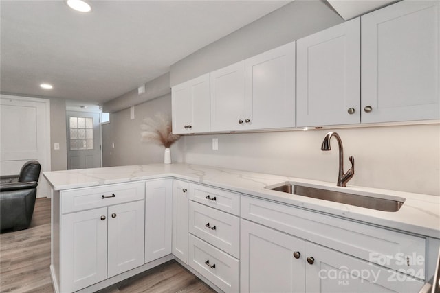 kitchen with white cabinetry, light stone counters, kitchen peninsula, light hardwood / wood-style flooring, and sink