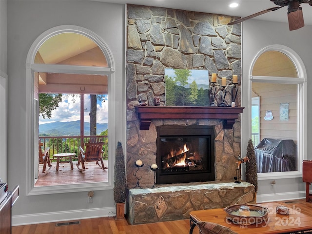 living room featuring wood-type flooring, a mountain view, a fireplace, and ceiling fan