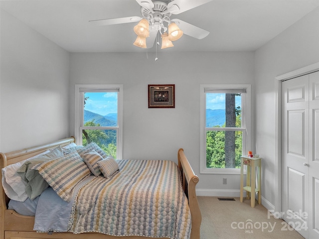 bedroom featuring multiple windows, ceiling fan, a closet, and light colored carpet