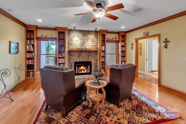 living room featuring ornamental molding, ceiling fan, a stone fireplace, and light hardwood / wood-style flooring