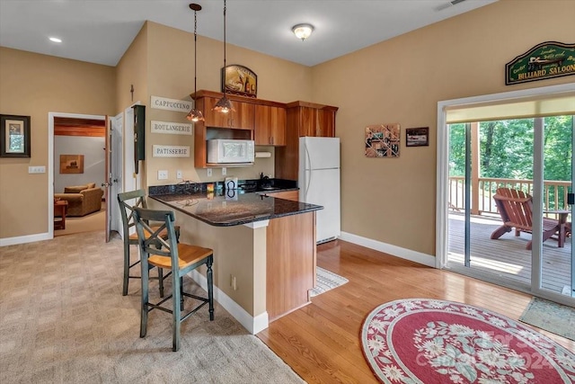 kitchen featuring white appliances, light hardwood / wood-style flooring, a breakfast bar, decorative light fixtures, and kitchen peninsula